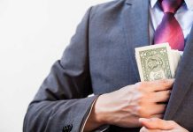 Person in suit putting dollars in jacket pocket