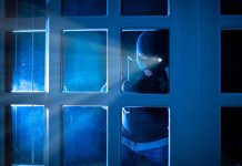 Masked figure peering through glass door at night
