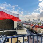 Polish flag over cityscape with buildings and cloudy sky