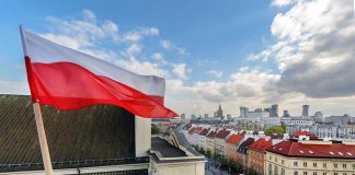Polish flag over cityscape with buildings and cloudy sky