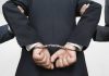 Person handcuffed in suitescorted by two others