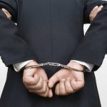 Person handcuffed in suitescorted by two others