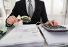 Person examining documents with magnifying glass and calculator.