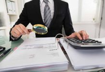 Person examining documents with magnifying glass and calculator.
