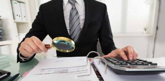 Person examining documents with magnifying glass and calculator.