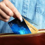 Hand holding credit cards over a brown purse