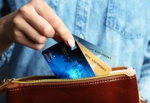 Hand holding credit cards over a brown purse