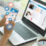 Person using smartphone and laptop with social media icons