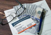 Medicare card glasses pen money on wooden table