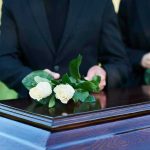 People placing white roses on a casket