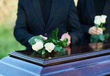 People placing white roses on a casket
