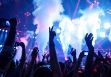 Crowd at a concert with hands raised and smoke effects in the background
