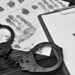 Handcuffs, fingerprint sheets, and clipboard on a desk.