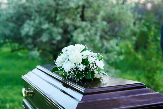 2361639877 Coffin with white flowers outdoors in green surroundings.