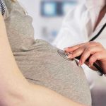 Doctor uses stethoscope on pregnant woman's belly.