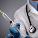 A doctor holding a syringe with a stethoscope around their neck