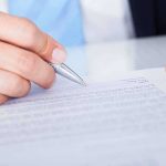 A hand holding a pen poised above a document for signing