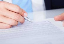 A hand holding a pen poised above a document for signing