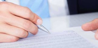 A hand holding a pen poised above a document for signing