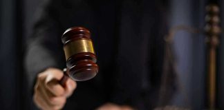 Hand holding gavel in courtroom setting.
