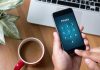 Typing privacy passcode on smartphone near laptop and coffee.