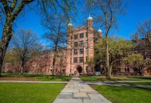 Historic university building surrounded by green grass and trees under a blue sky
