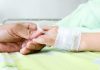 A person holding the hand of a patient with an IV in a hospital bed