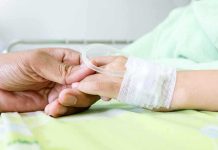 A person holding the hand of a patient with an IV in a hospital bed
